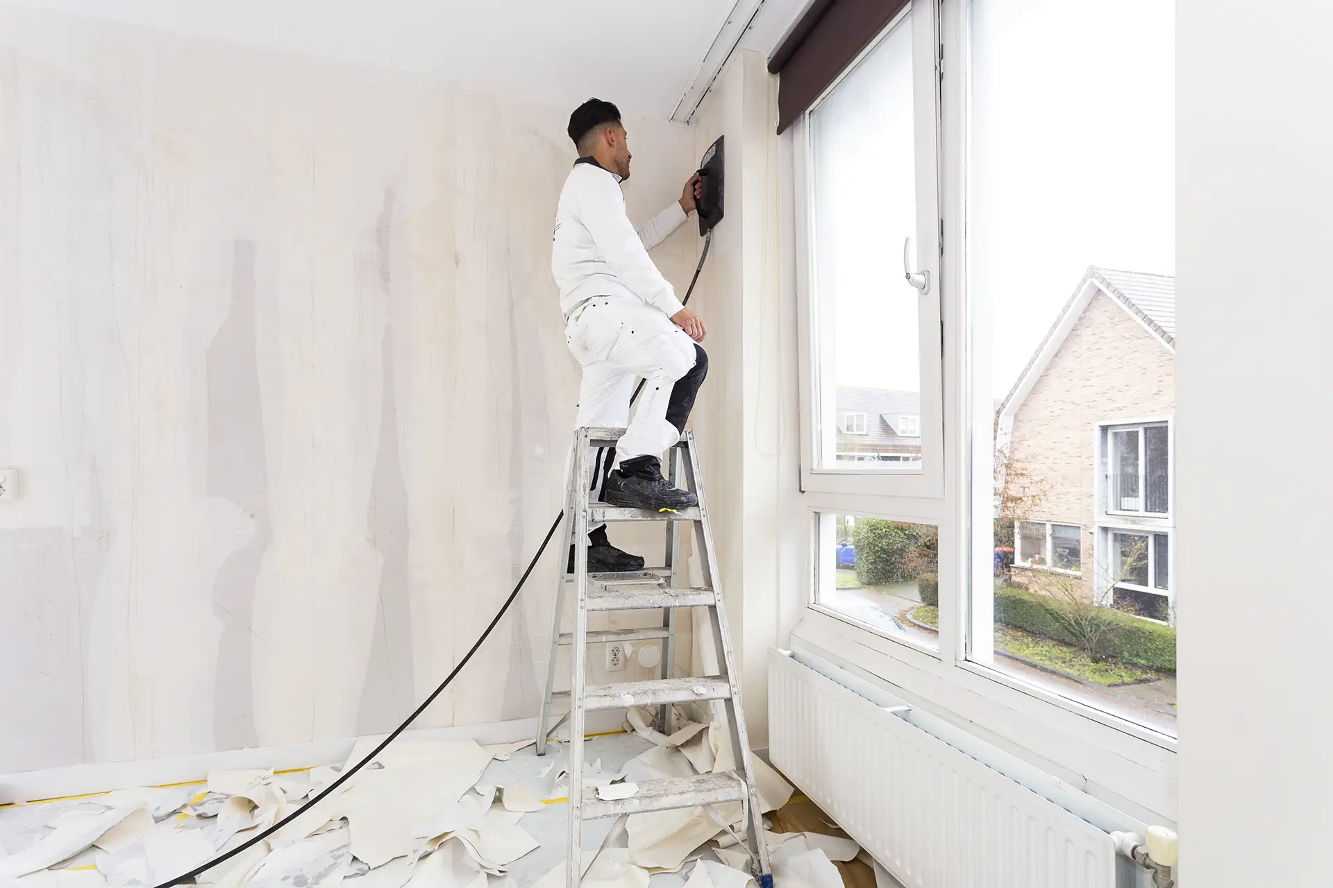 Een ervaren behanger van renovliesin Ede verwijdert oud behang om de muren klaar te maken voor een strakke renovlies afwerking.