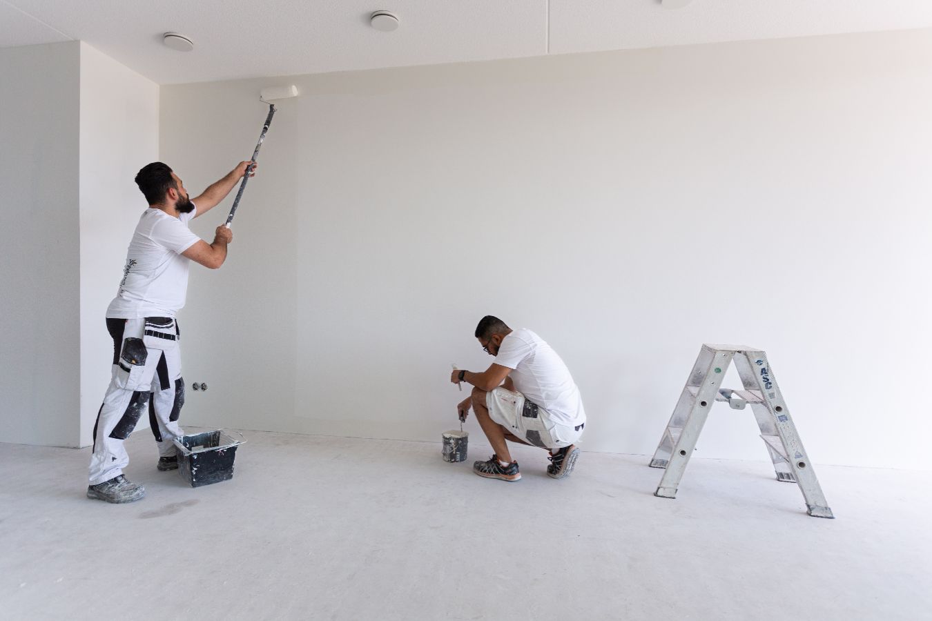 Twee vakmannen werken samen aan het afwerken van een witte glasvlies muur.