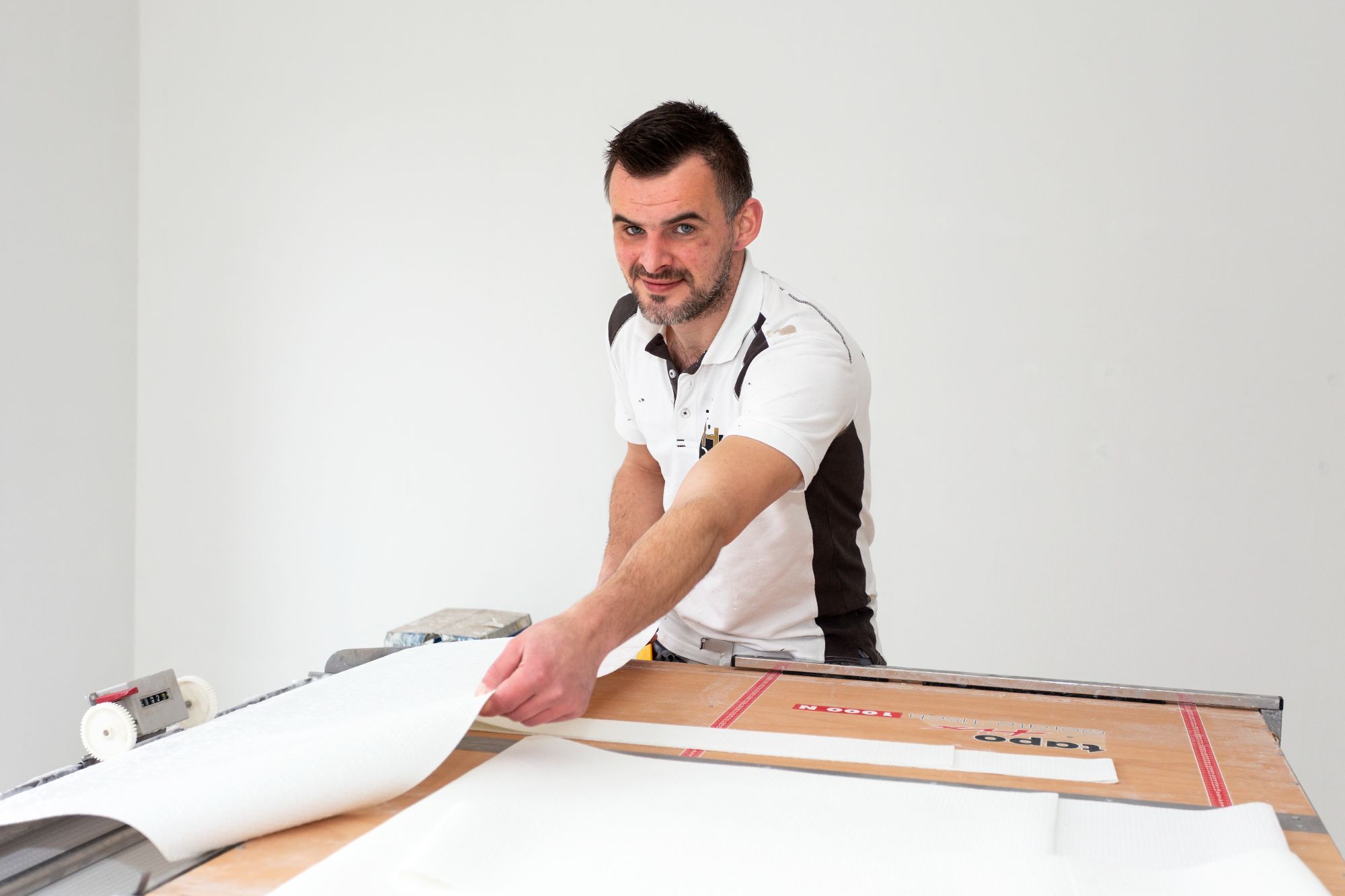 Een vakman van Renovlieskoning snijdt glasvlies behang op maat voor een strakke wandafwerking