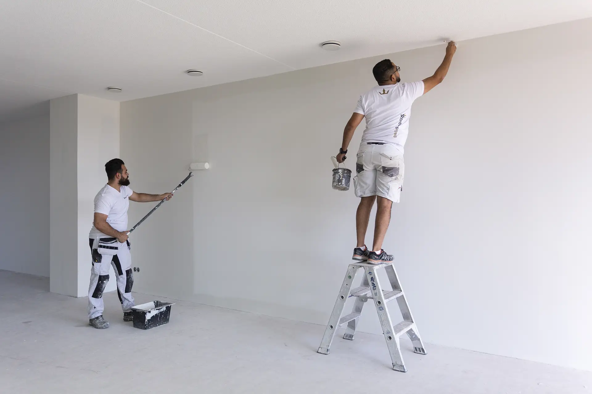 Twee schilders werken samen aan het schilderen van een witte renovlies muur.