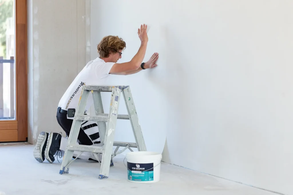 Vakman brengt renovlies behang aan op een muur in een nieuwbouwwoning – alternatief voor stucen bij nieuwbouw
