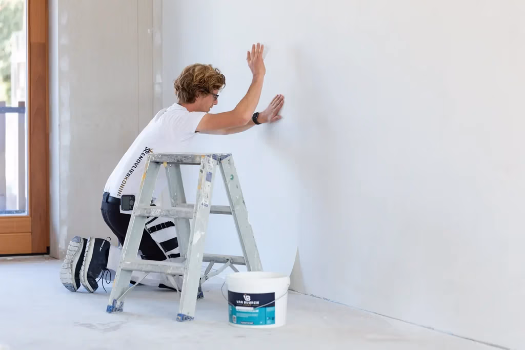 Renovlies behanger nauwkeurig bezig met het behangen van een oneffen muur